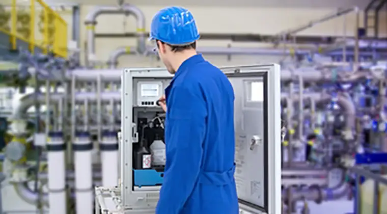 Person, wearing a blue uniform and a blue safety helmet, interacting with an electrical panel. The environment suggests that this is inside a factory or processing plant where manufacturing or other industrial activities are carried out.