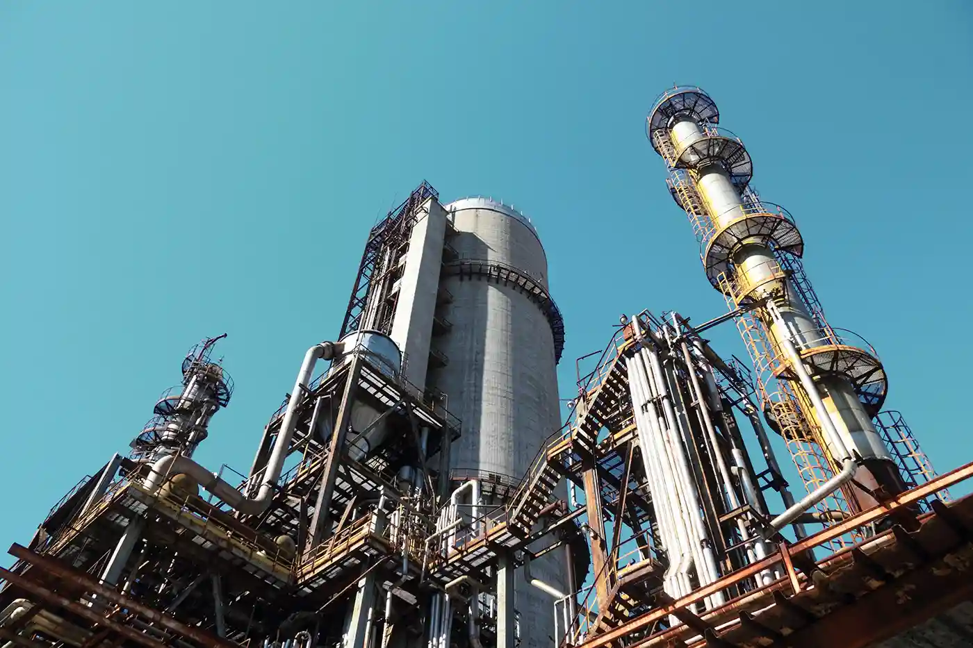 Photo of an industrial plant with tall towers and pipes against a clear blue sky