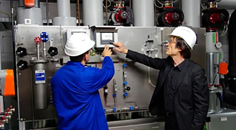 Two professionals in safety helmets inspecting a control panel in an industrial setting
