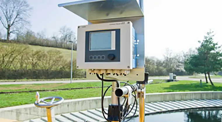 A computer monitor sitting on a metal box next to a sewage treatment plant basin.