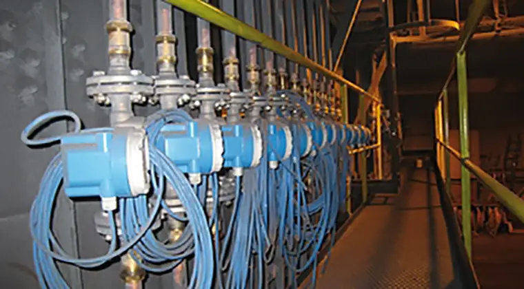 A series of industrial valves and blue cables organized along a wall in a dimly lit room.